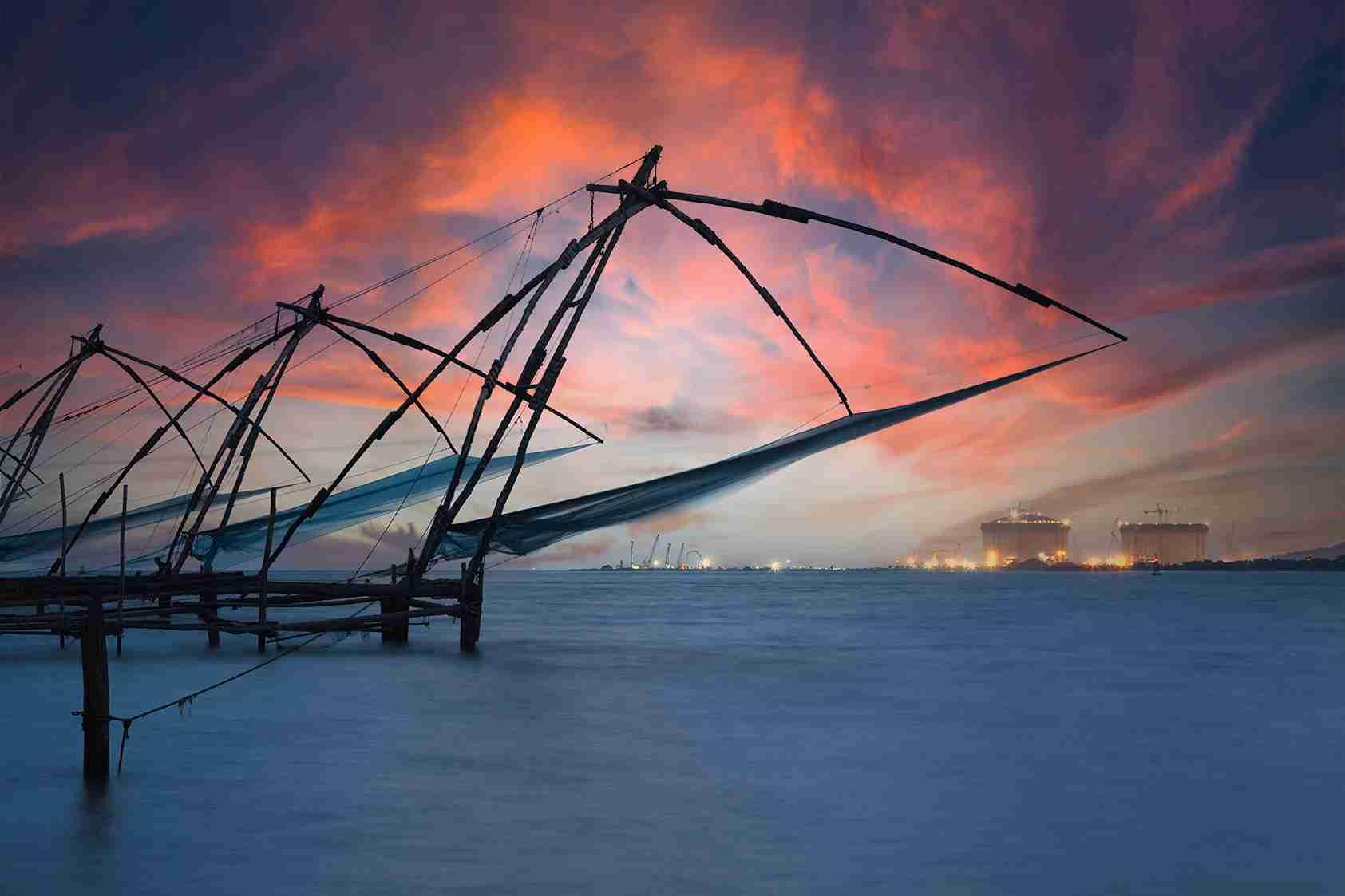 Traditional Chinese fishing nets at sunset in Fort Kochi, Kerala with an industrial skyline in the background
